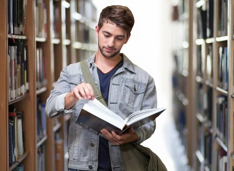 junger Mann in Bibliothek mit Buch in den Händen