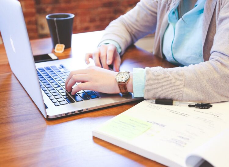 Frau mit Buch, Laptop und Teetasse auf dem Tisch